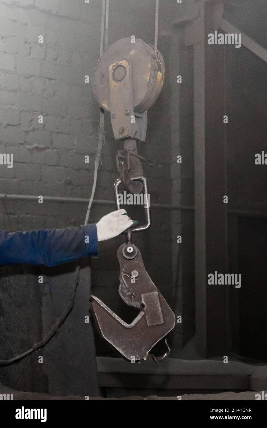 La mano di un uomo che lavora prende un meccanismo di sollevamento industriale a gancio nell'officina di fabbrica. Foto Stock