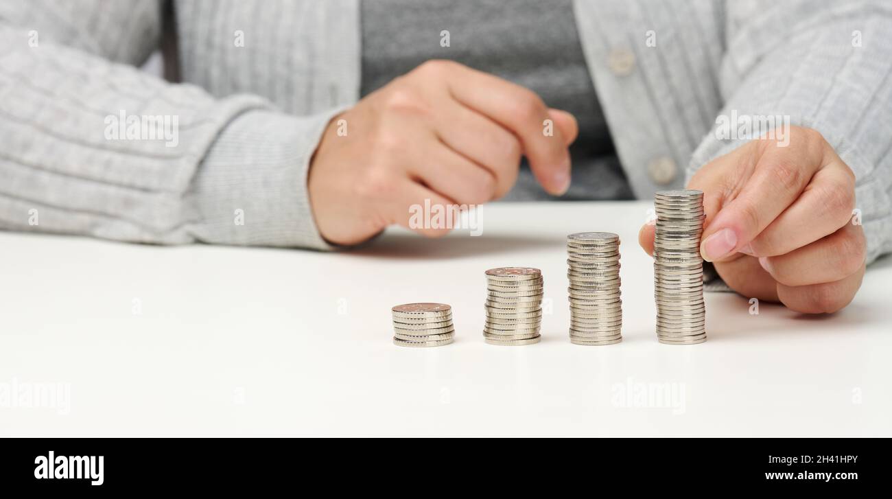 La donna è seduta al tavolo e una pila di monete sul tavolo. Calcolo delle spese e dei redditi, delle sovvenzioni, delle imposte Foto Stock