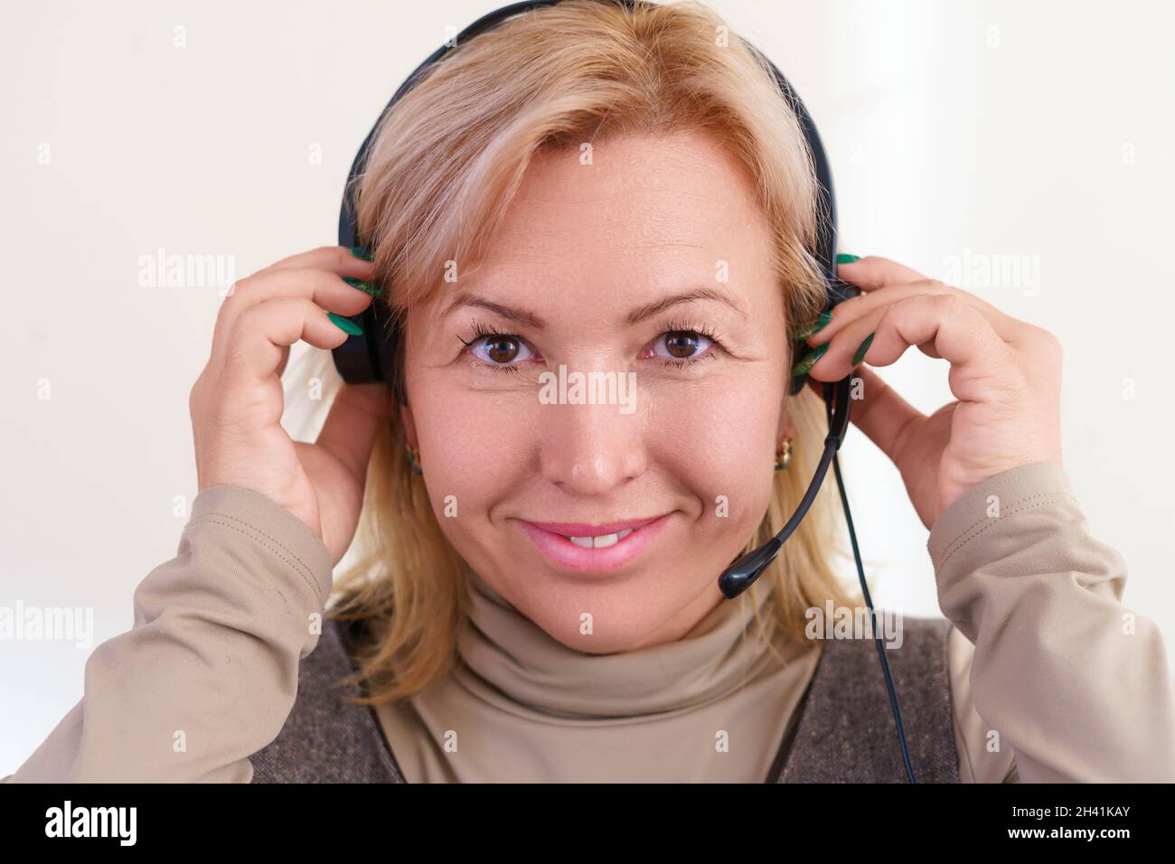 Ritratto in primo piano di una donna caucasica sorridente di mezza età che regola una cuffia sulla testa. Foto Stock