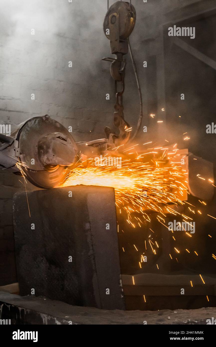 L'attrezzatura di molatura pesante sospesa su una catena con un gancio elabora e pulisce i tubi in cemento armato in ghisa nell'officina di una p. Industriale Foto Stock