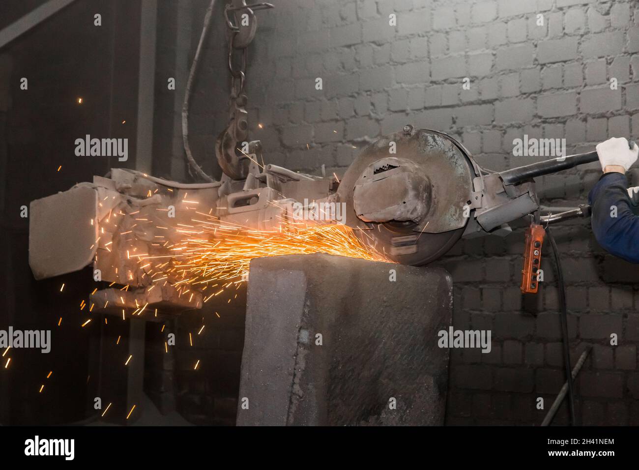 L'attrezzatura di molatura pesante sospesa su una catena con un gancio elabora e pulisce i tubi in cemento armato in ghisa nell'officina di una p. Industriale Foto Stock