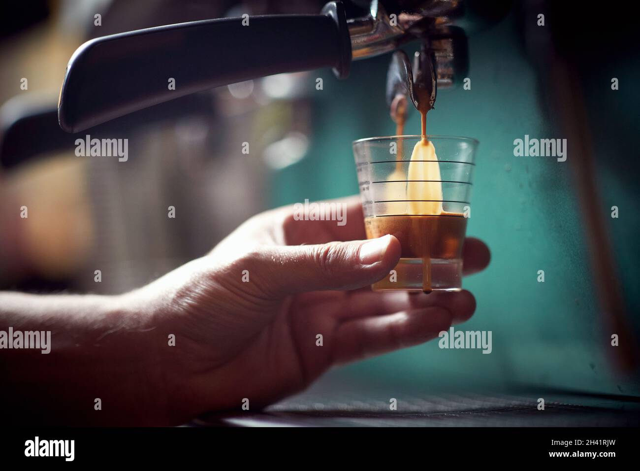 Un barman tiene un bicchiere e lo riempie di bevanda aromatica e fragrante in un apparecchio espresso. Caffè, bevande, bar Foto Stock