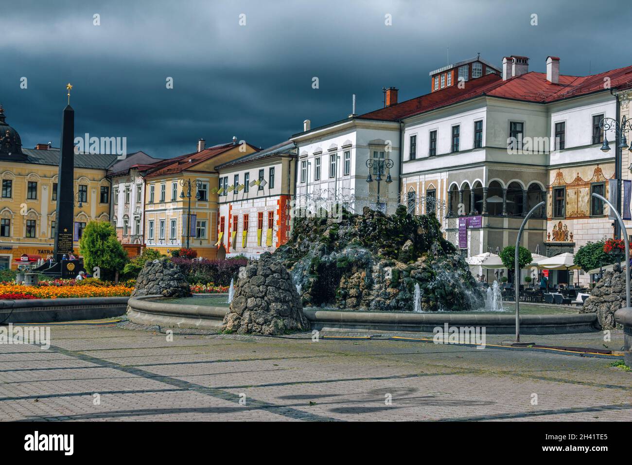 Banska Bystrica, Slovacchia – 15 agosto 2021: Vista di Piazza SNP – colorati edifici storici, fontana e monumento, nuvole tempeste grigie. Foto Stock