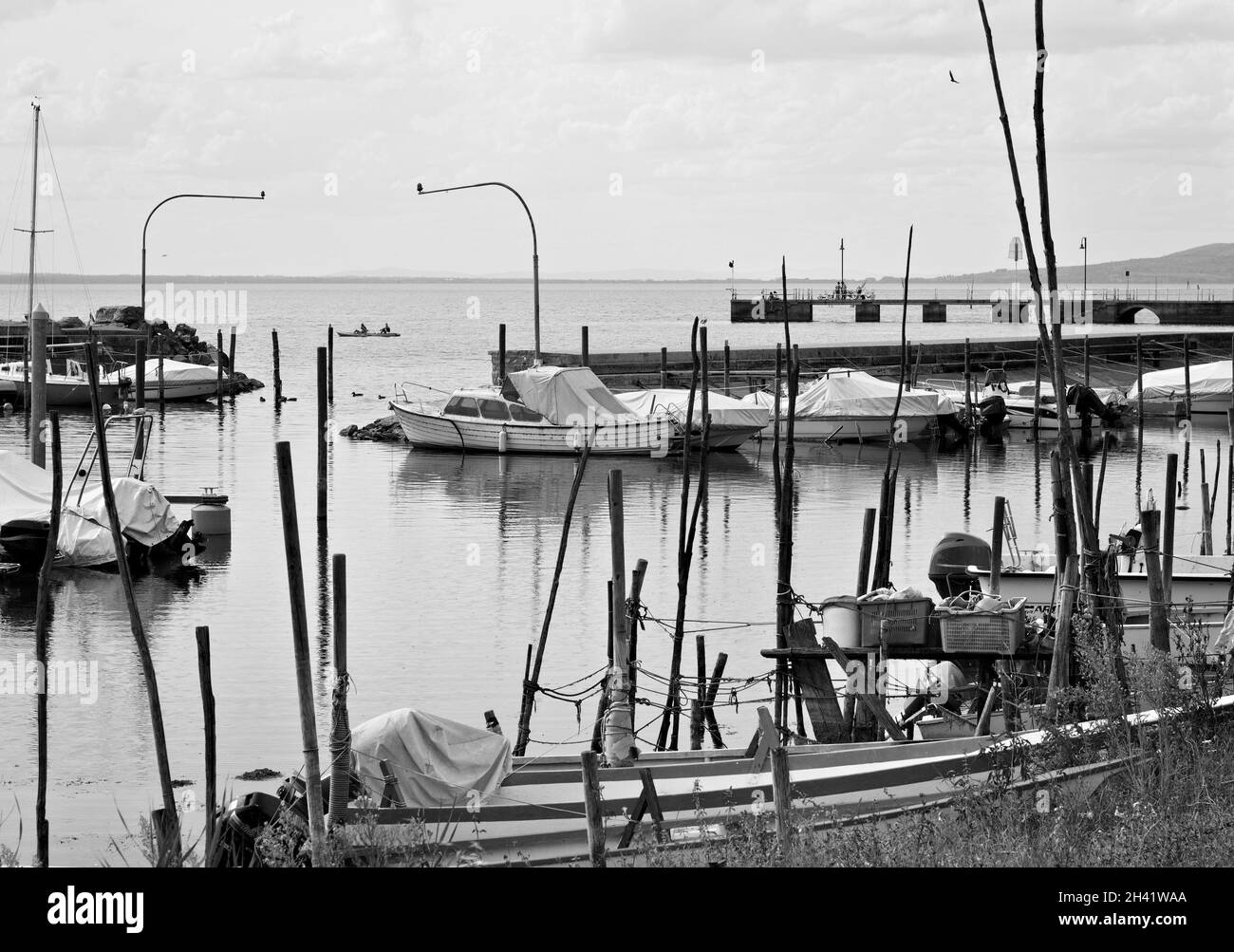 Piccole imbarcazioni a motore ormeggiate su pali di legno del molo di un piccolo porto sul Lago Trasimeno (Umbria, Italia, Europa) Foto Stock