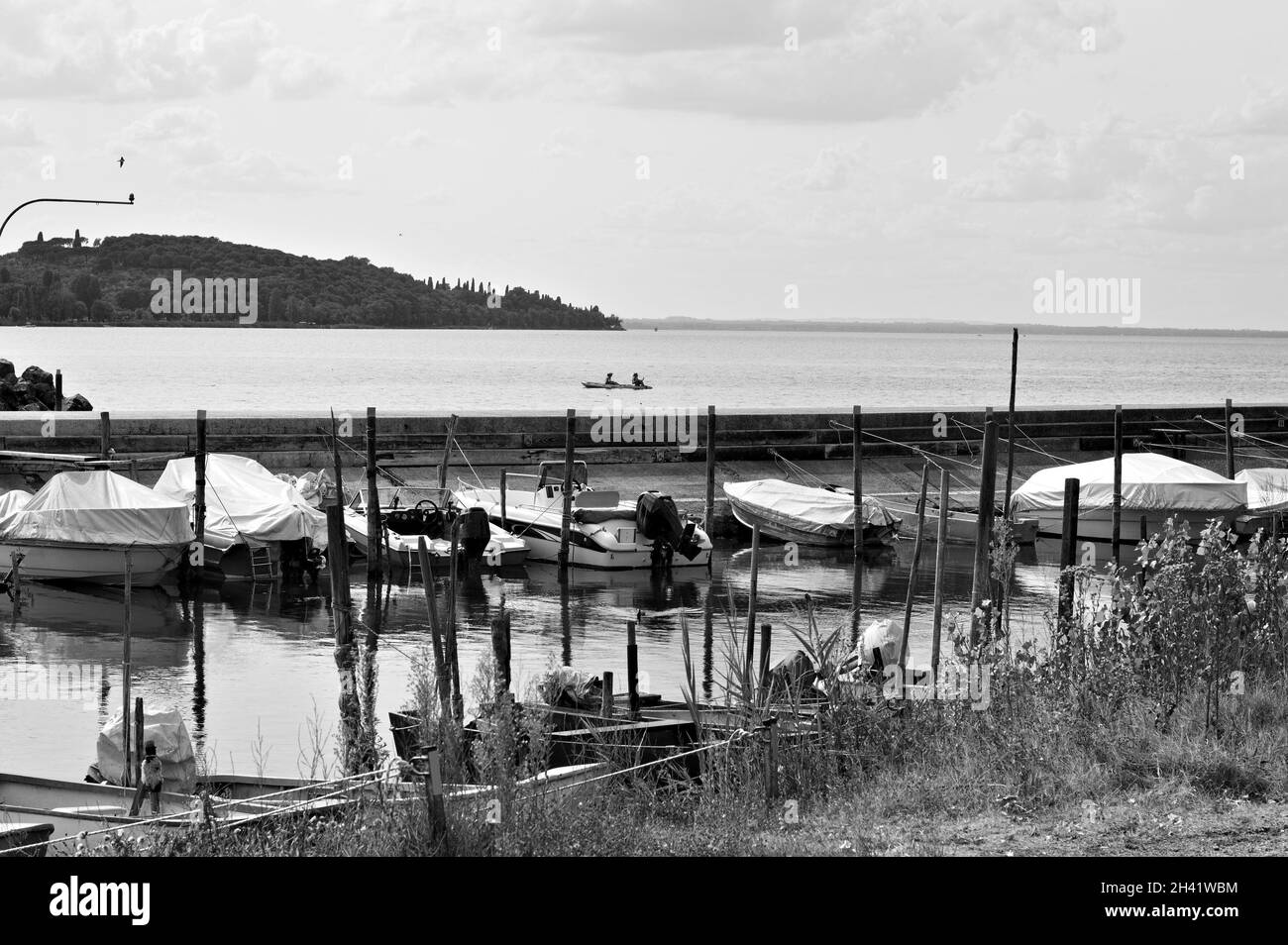 Piccole imbarcazioni a motore ormeggiate su pali di legno del molo di un piccolo porto sul Lago Trasimeno (Umbria, Italia, Europa) Foto Stock