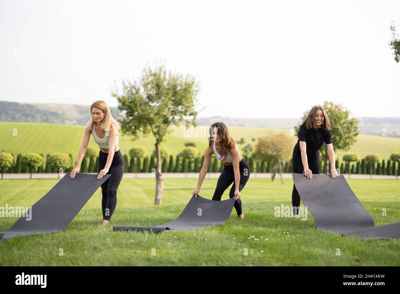 Girlfriends mettere i tappetini fitness sul prato verde Foto Stock