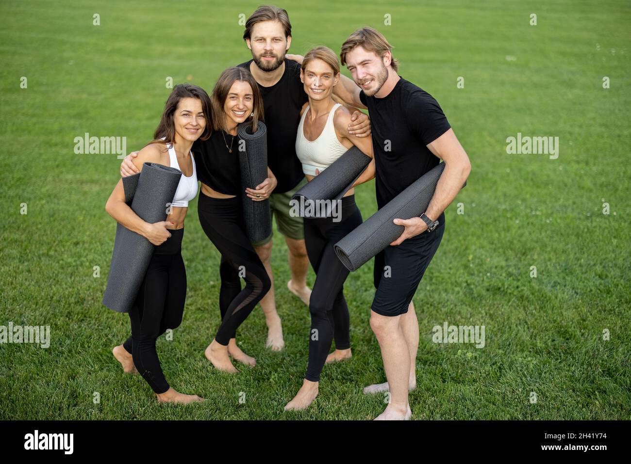 Le persone con materassini per il fitness si trovano in un prato verde Foto Stock