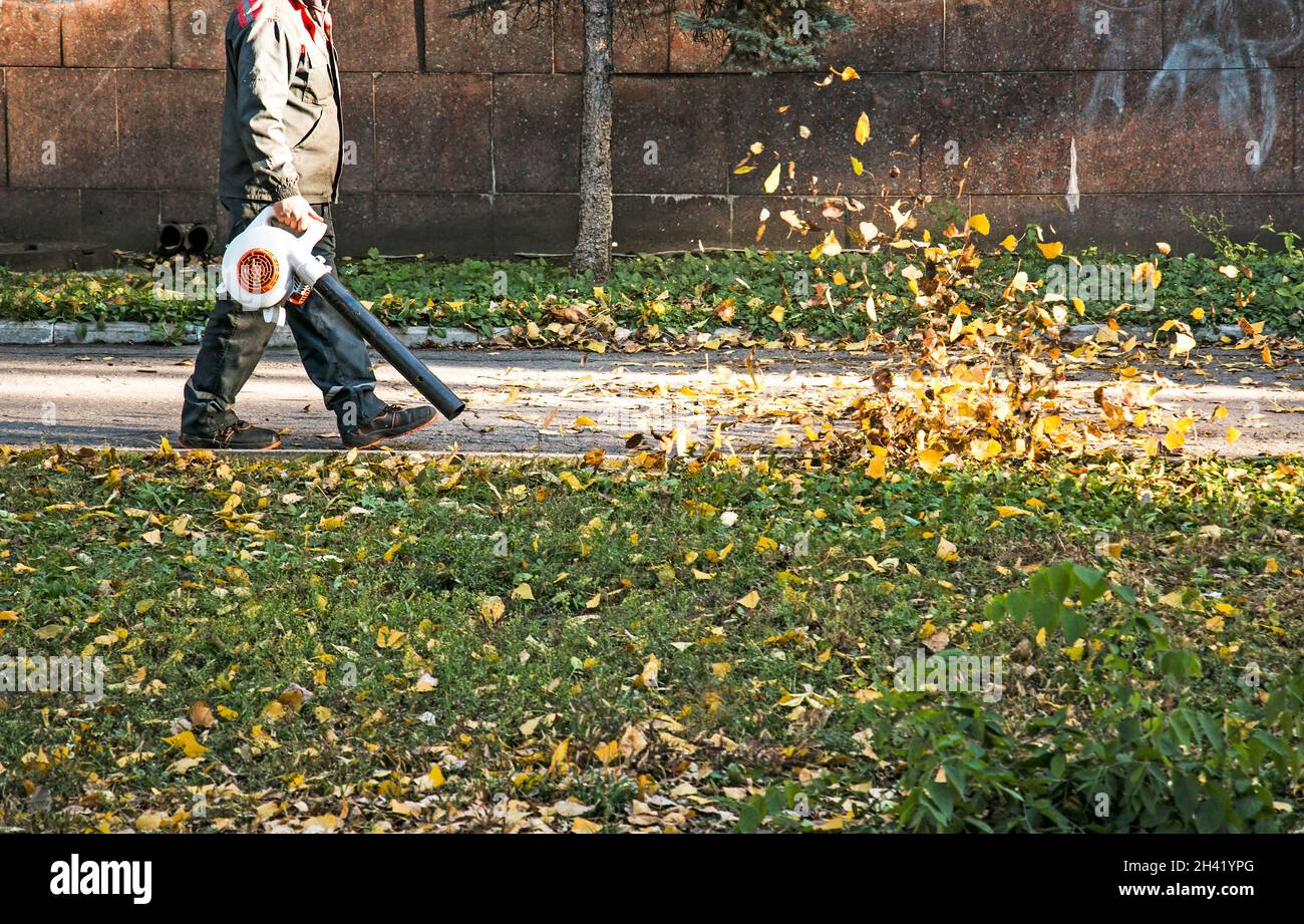 Pulizia foglie secche con un mulino a vento. Un lavoratore municipale pulisce il parco cittadino. Preparazione dei parchi cittadini per l'inverno. Foto Stock