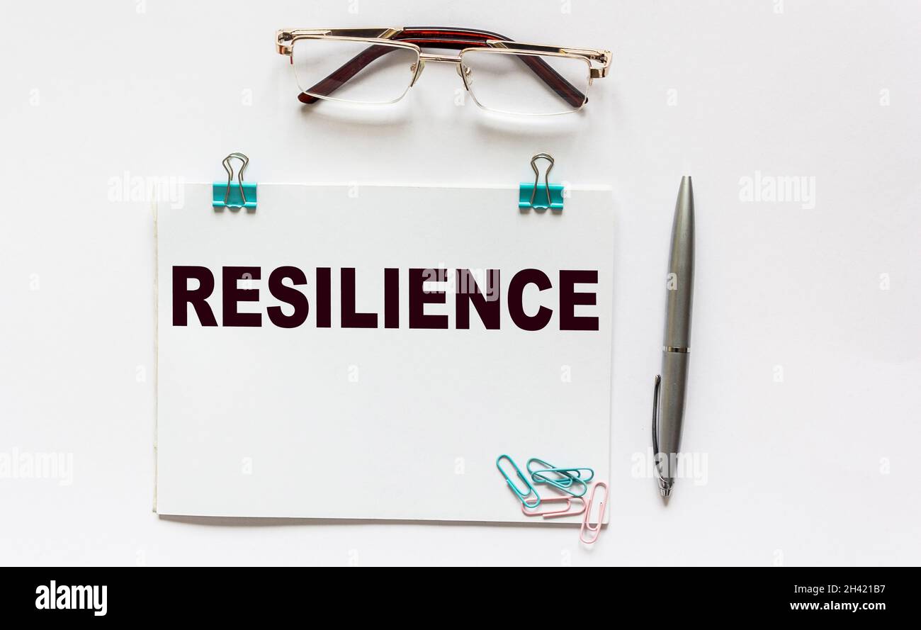 Resilienza, il testo è scritto su un notebook, accanto agli occhiali, una penna e clip di carta su uno sfondo bianco Foto Stock