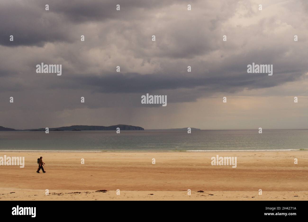 Guardando al mare a Polin Bay, Sutherland, Scozia, attraverso la sabbia con nuvole, promontori, l'orizzonte, e un maschio a piedi sulla spiaggia Foto Stock