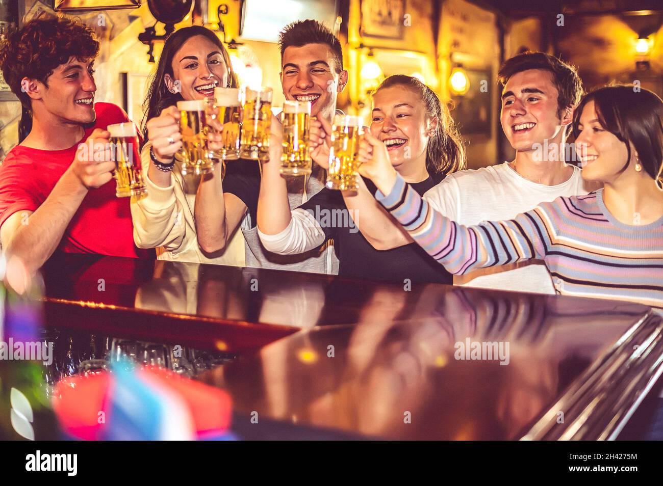 Gruppo di persone felici che bevono e tostano la birra al banco del bar - bei amici adolescenti sorridendo mentre si stringono tazze di birra alla spina - amicizia Foto Stock