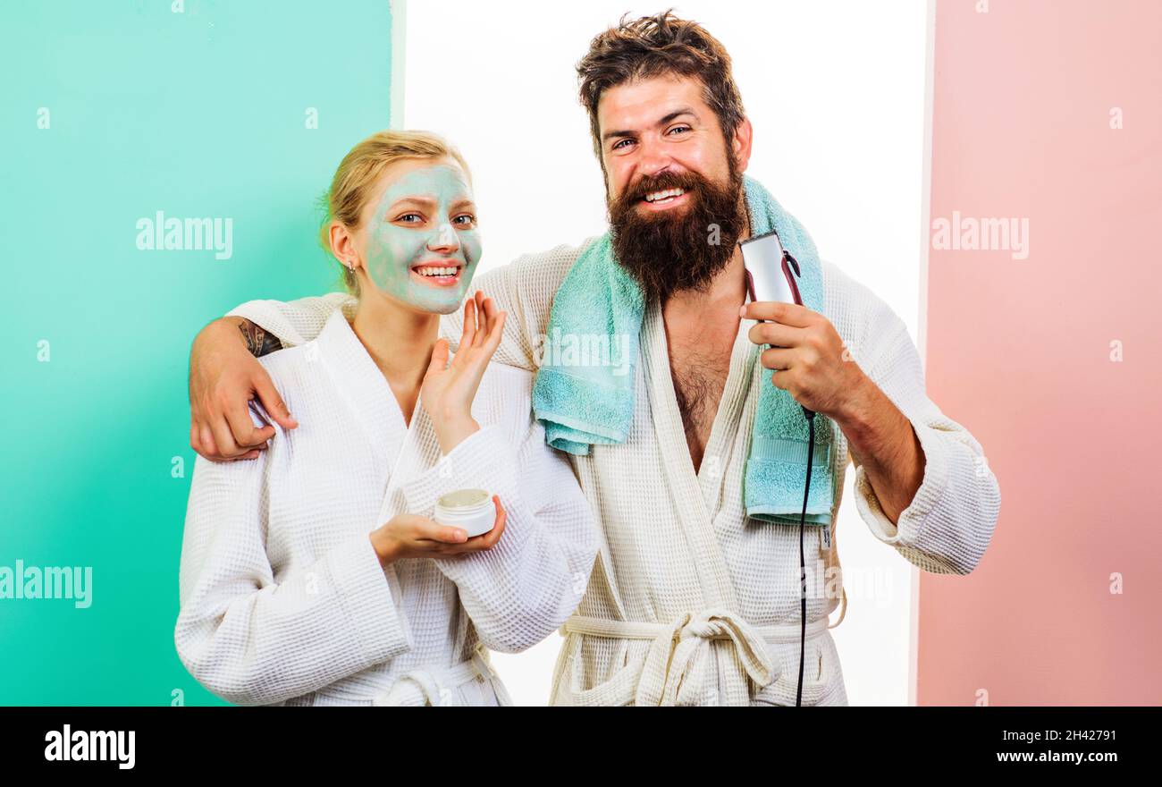 Marito e moglie in bagno. Uomo bearded con rasoio elettrico. Donna con maschera cosmetica facciale. Procedure del mattino. Vita familiare. Foto Stock