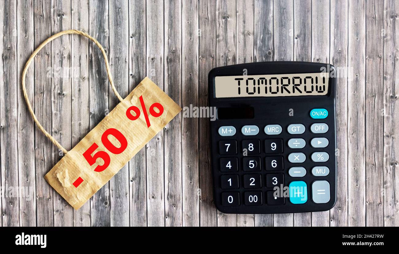 Concetto di marketing: VENDITA 50 OFF scritto su etichetta marrone e tavolo in legno. La calcolatrice visualizza LA parola DOMANI Foto Stock