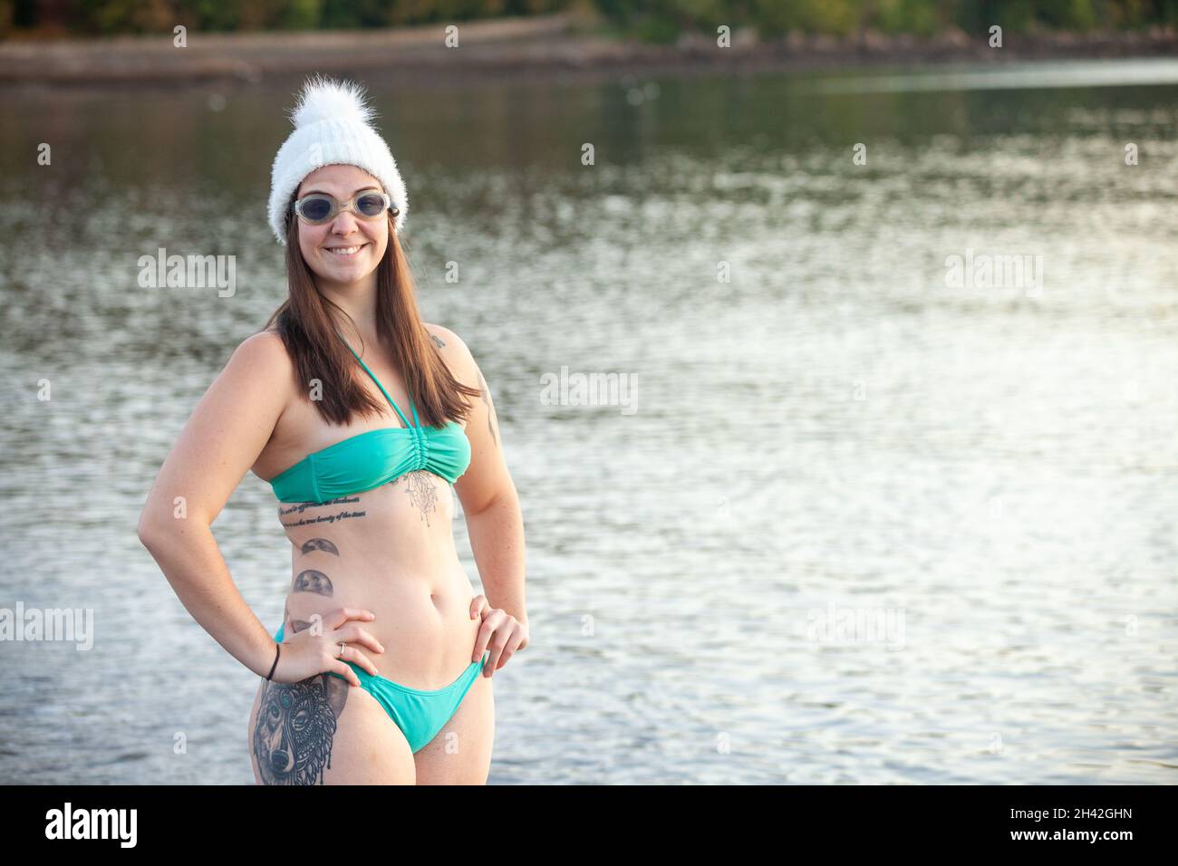 Una giovane donna che indossa un bikini in piedi vicino al bordo del mare e indossa un cappello di lana pronto per una nuotata degli inverni Foto Stock