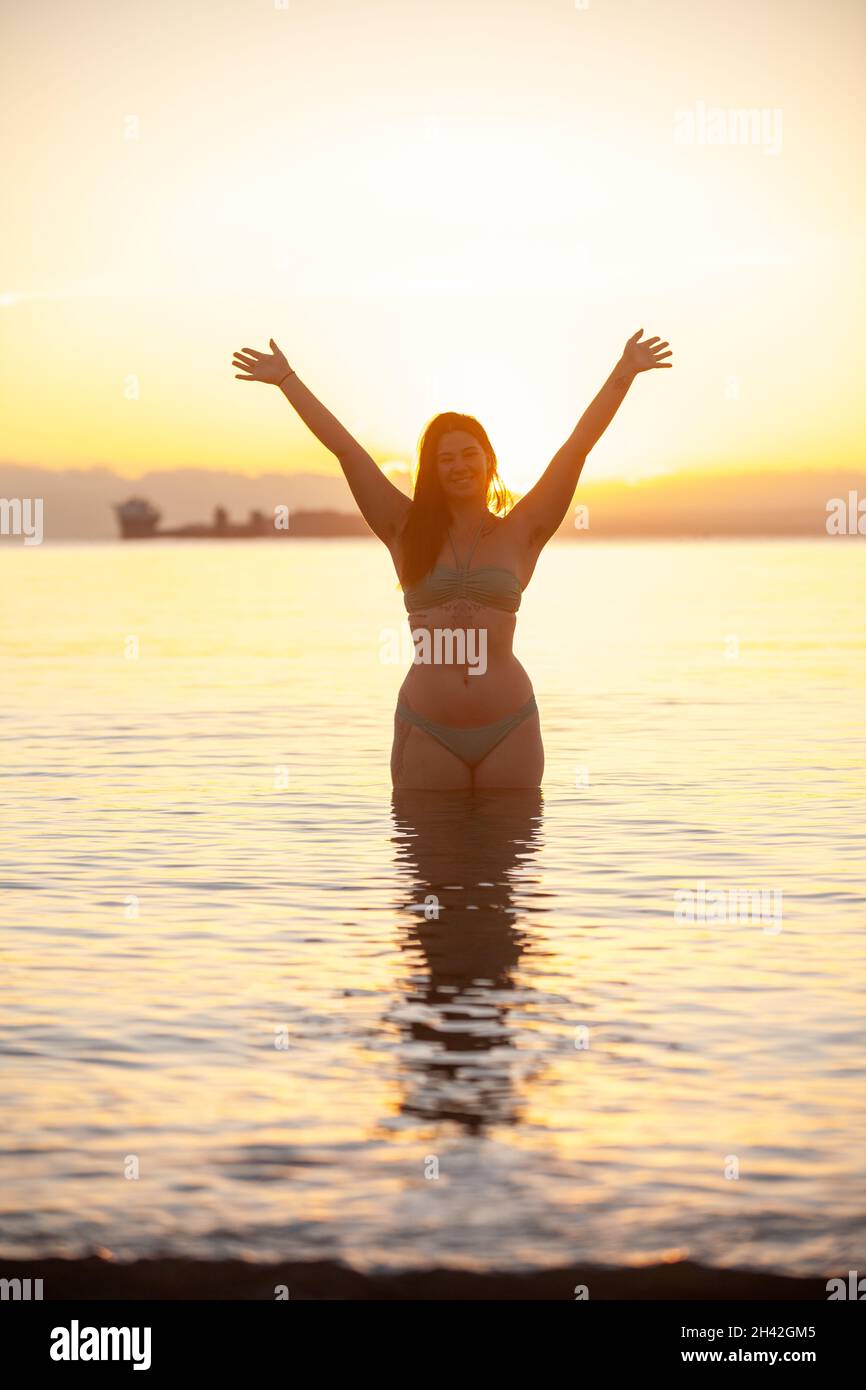 Una donna in piedi in mare in una fredda mattinata di ottobre accoglie l'alba. Foto Stock