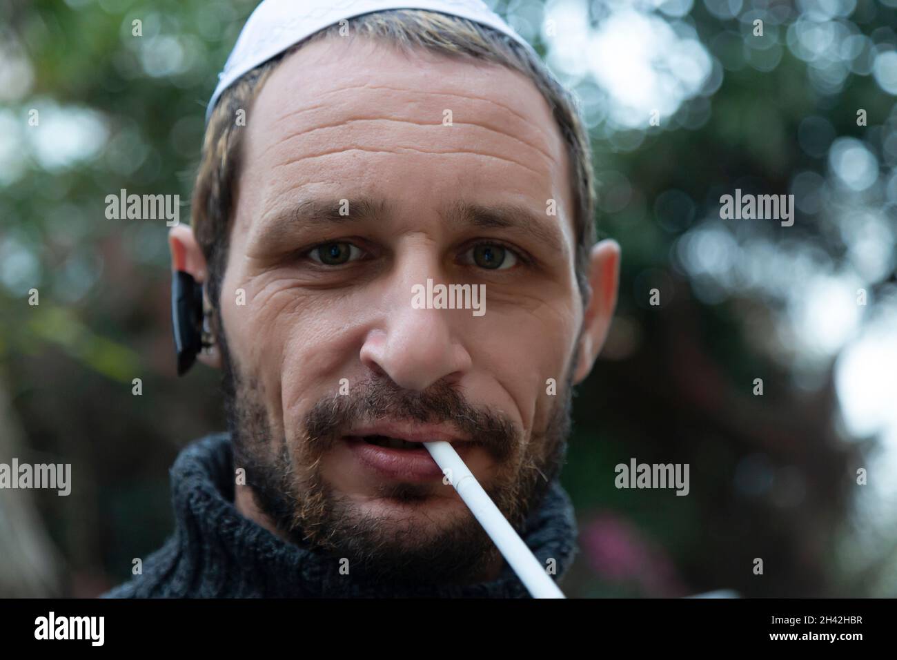 Uomo ebreo che indossa kippah in ebraico o yarmulke con alberi verdi sullo sfondo, barba che indossa una felpa nera. Ritratto di un uomo di mezza età con Foto Stock