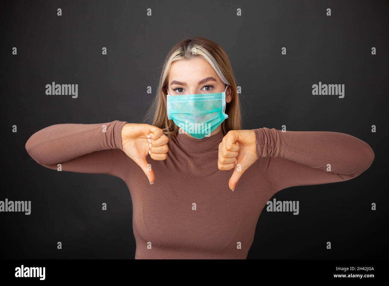 Ritratto di donna giovane delusa che indossa una maschera in piedi con i pollici giù Foto Stock