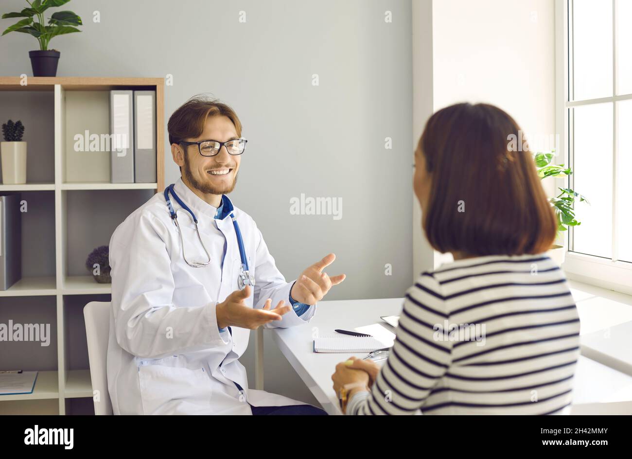 Sorridente medico maschile amichevole dice al suo paziente buone notizie alla riunione in ospedale ufficio. Foto Stock
