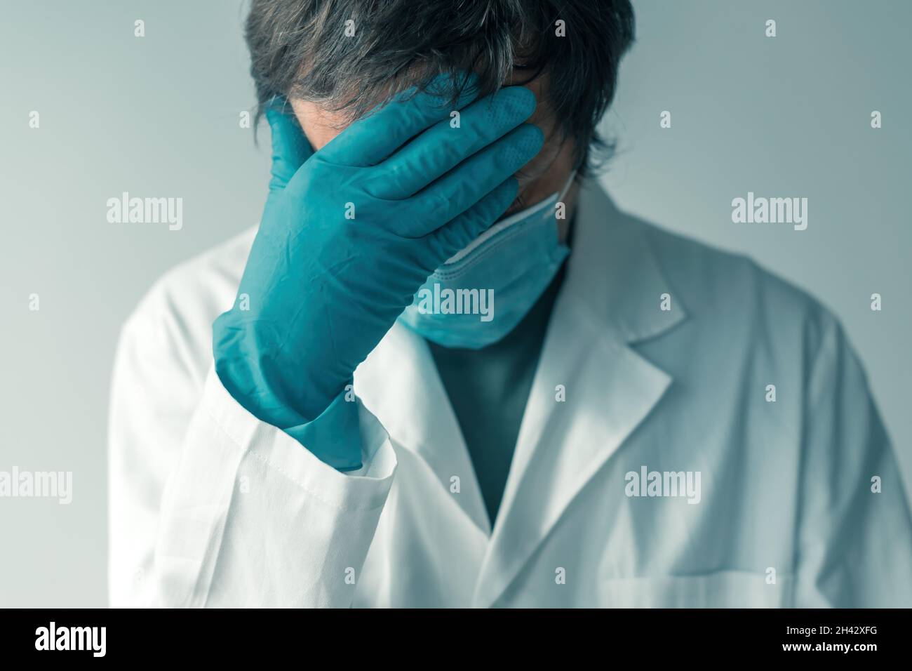 Preoccupato medico con guanti protettivi e maschera viso con mano di copertura del viso, fuoco selettivo Foto Stock