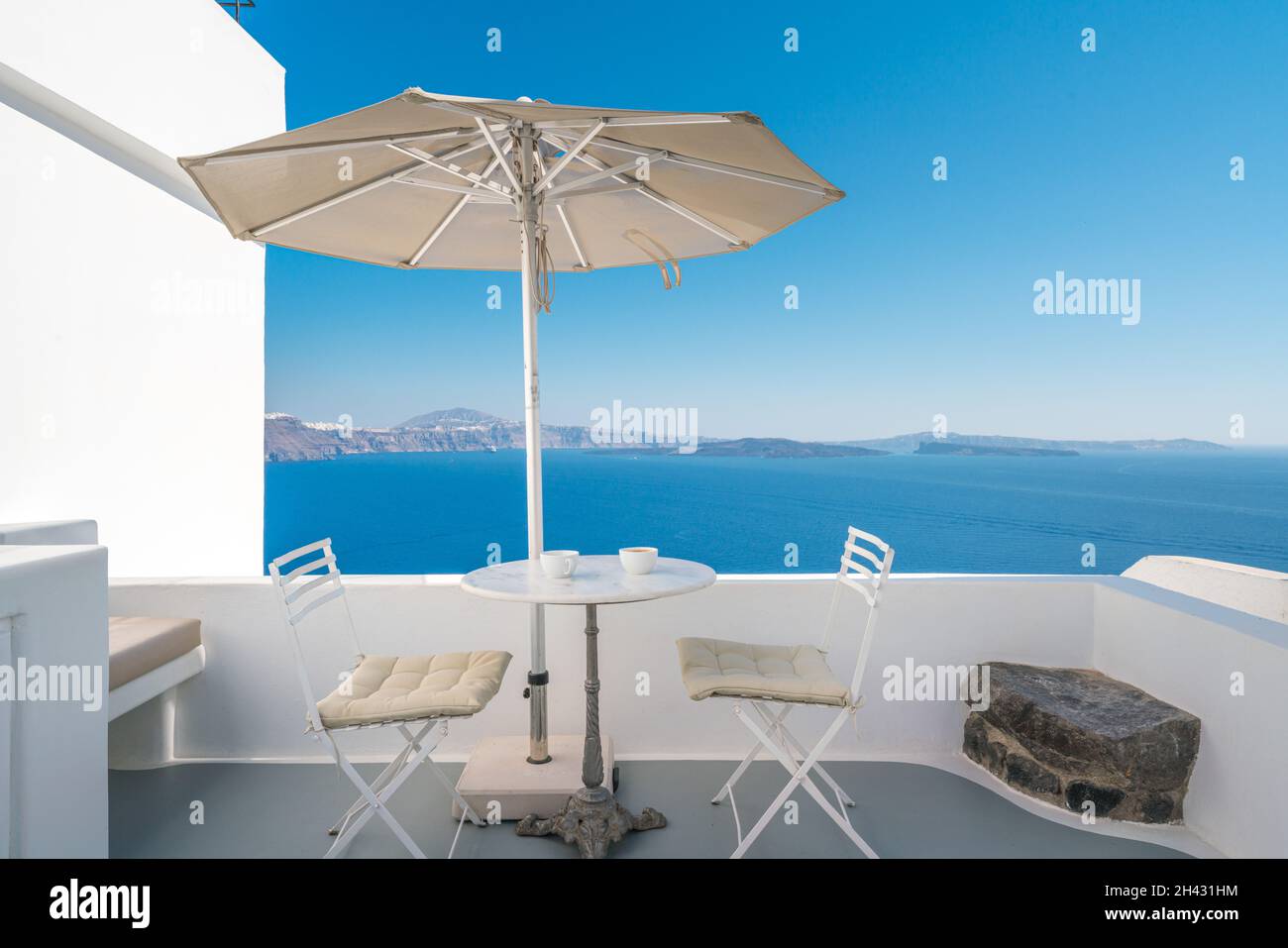 Terrazza all'aperto con ombrellone, scrivania e sedie contro i blu marino sull'isola di Santorini, Grecia Foto Stock