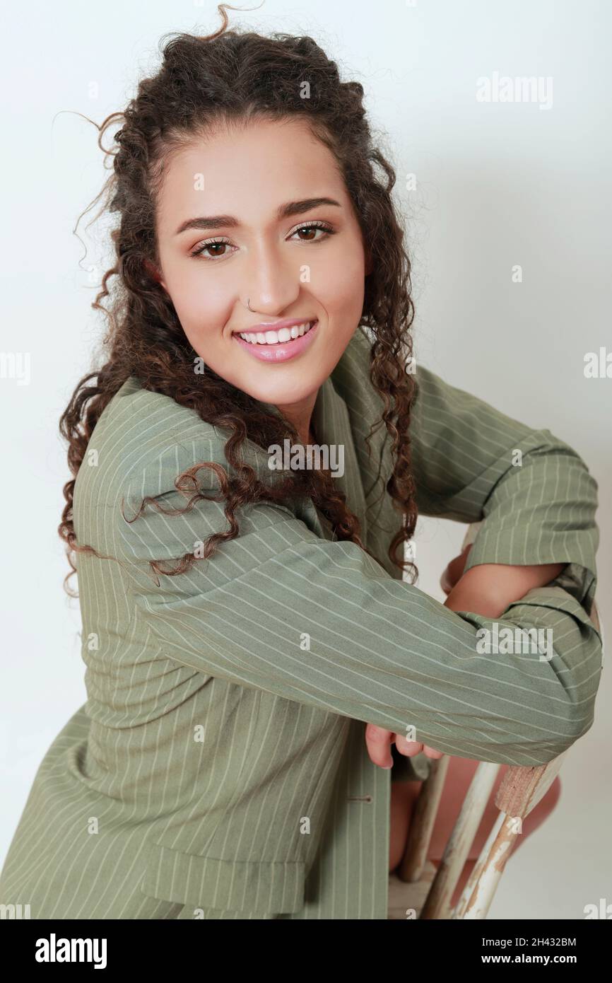 ritratto di latina ragazza con blazer posto su una sedia guardando la macchina fotografica con bel sorriso Foto Stock