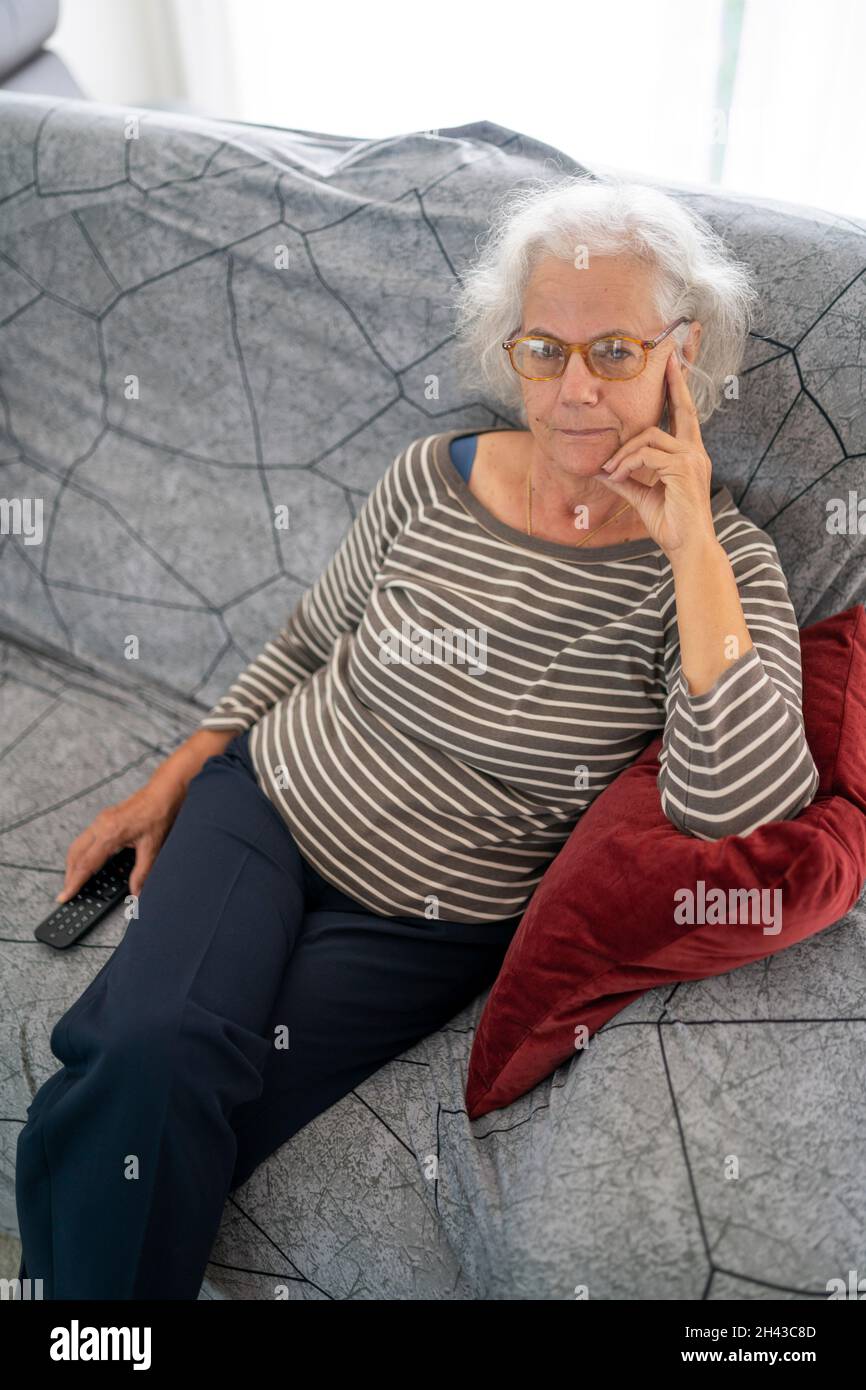 Ritratto di una donna matura seduta sul suo divano a casa Foto Stock