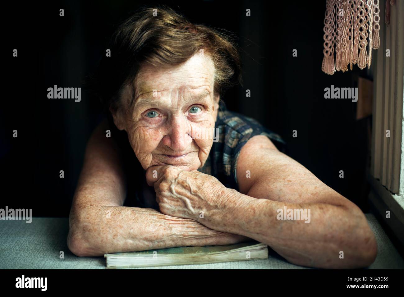 Ritratto di una vecchia donna seduta a un tavolo in casa. Foto Stock