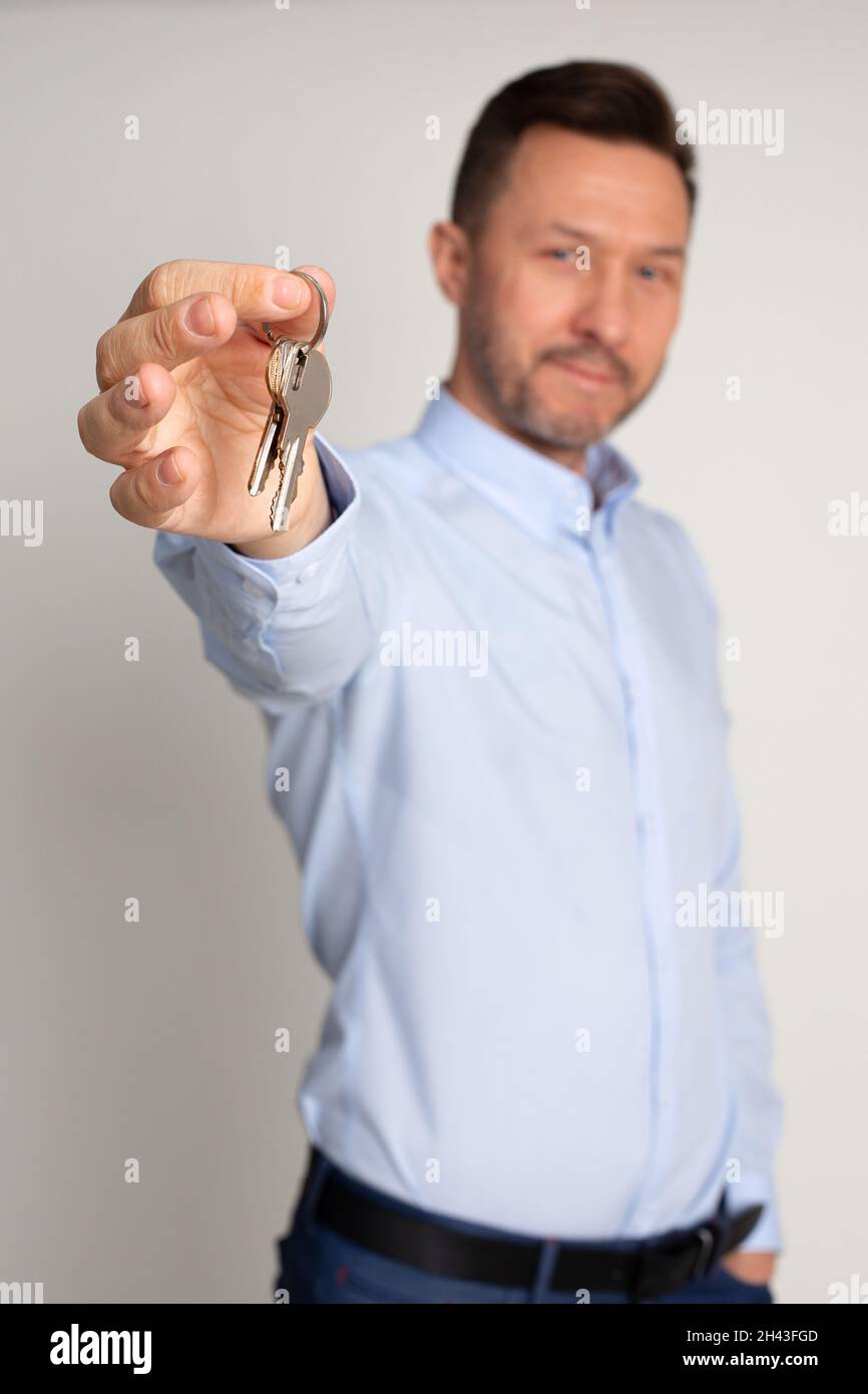 Foto verticale del responsabile del dipendente in camicia dell'agenzia immobiliare tiene in mano le chiavi degli appartamenti. Comprare o affittare casa. L'uomo è felice di diventare Foto Stock
