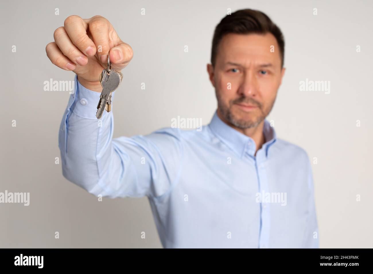 Foto del manager dipendente in camicia di agenzia immobiliare tiene in mano le chiavi degli appartamenti. Comprare o affittare casa. L'uomo è felice di diventare proprietario di casa Foto Stock