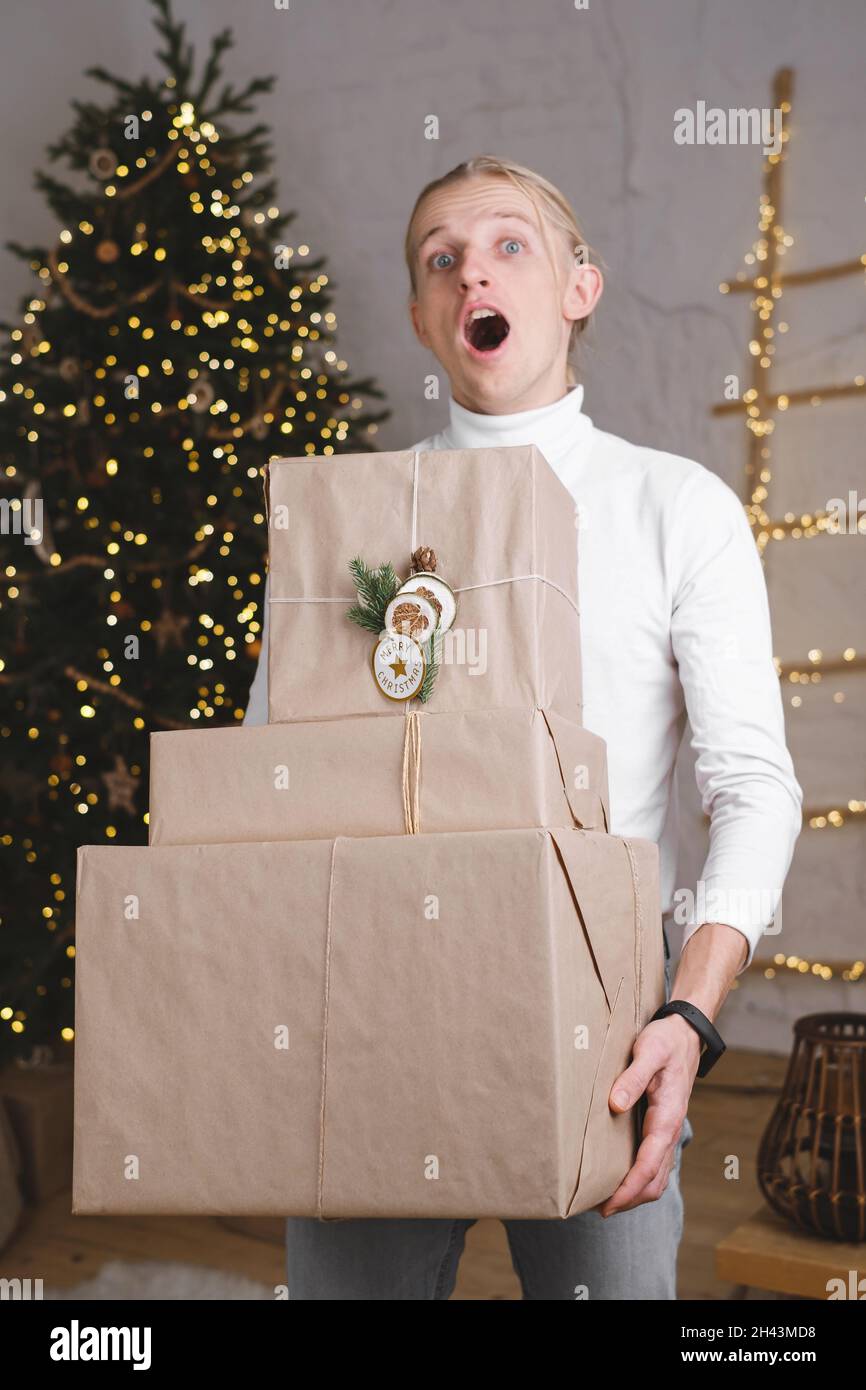 Uomo divertente di fronte all'albero di Natale pronto per la celebrazione  con grandi regali giganti, persona emozionale con eco presente. Chiamare  gli amici Foto stock - Alamy