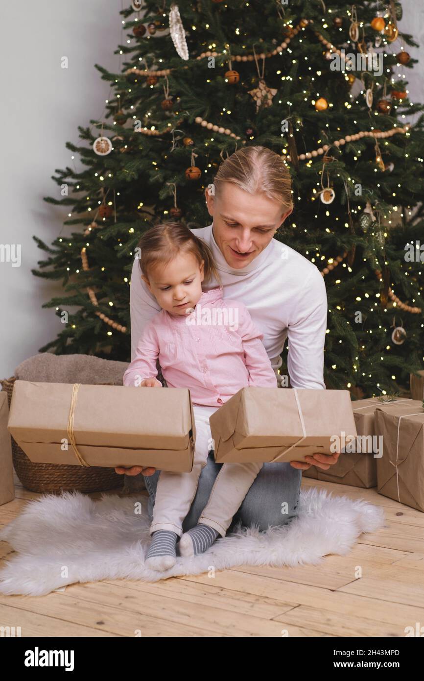 Padre con il bambino che si prepara per il Natale, confezione scatole regalo vicino albero. Famiglia felice sognando di celebrazioni e regali a elegante Foto Stock