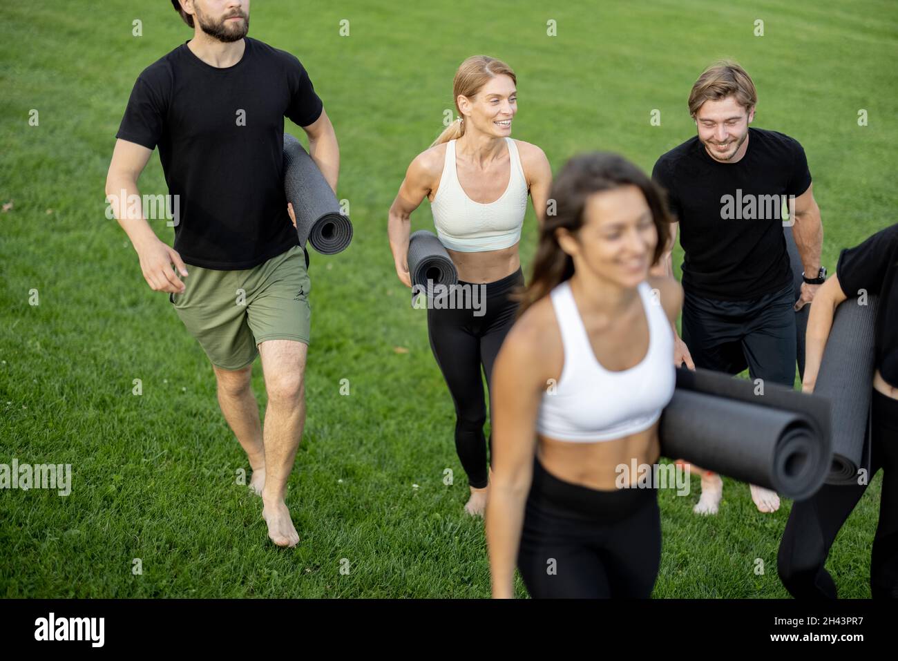 Persone che camminano con materassini fitness sul prato verde Foto Stock