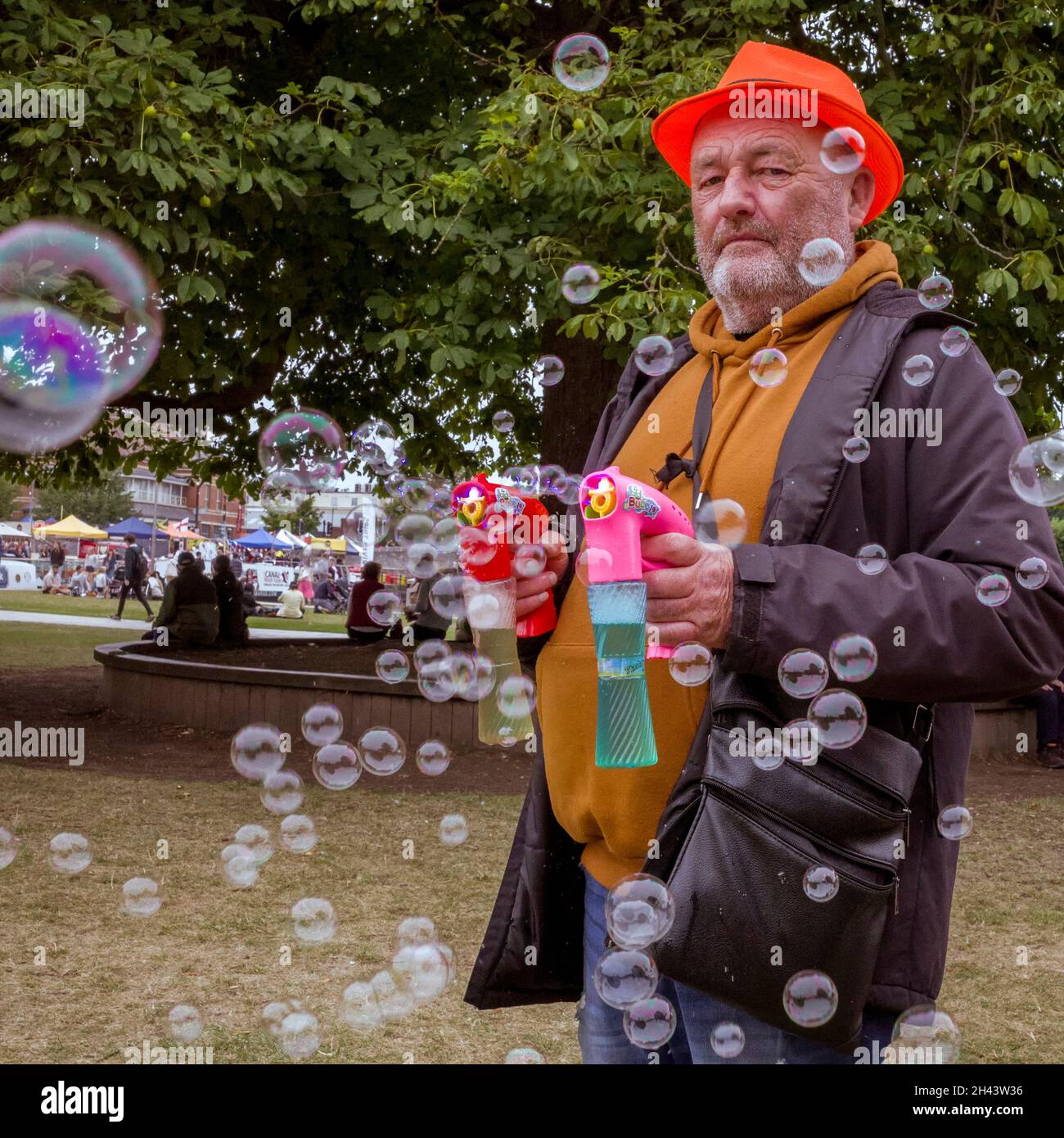 Un uomo in piedi in un parco spara bolle da due pistole bolla. Foto Stock