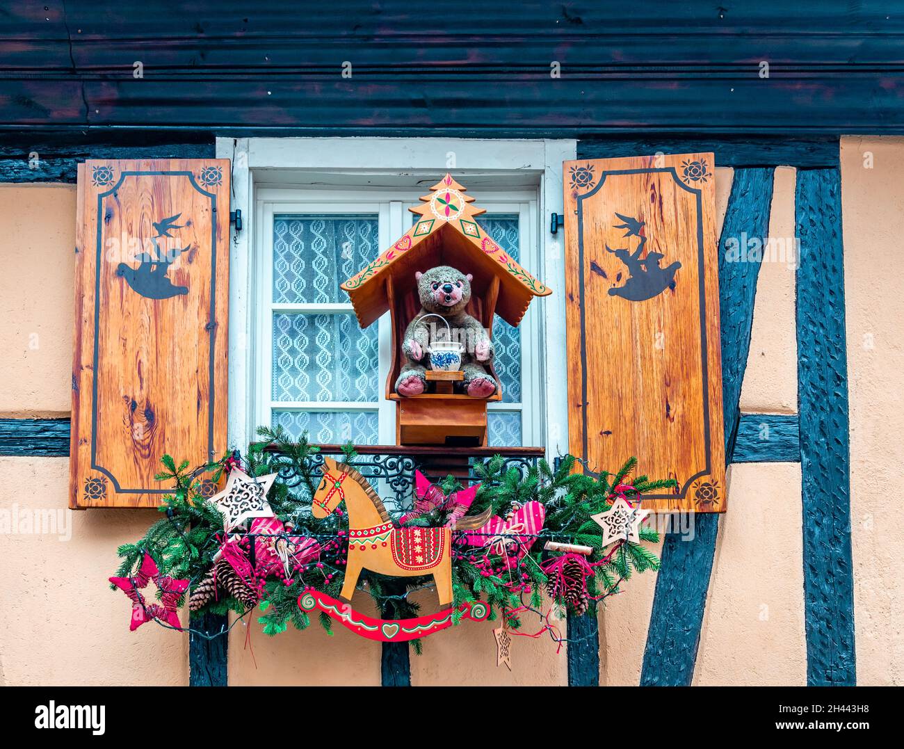 Una finestra con persiane in legno e un orsacchiotto con decorazioni natalizie. Ribeauville, Alsazia, Francia. Foto Stock