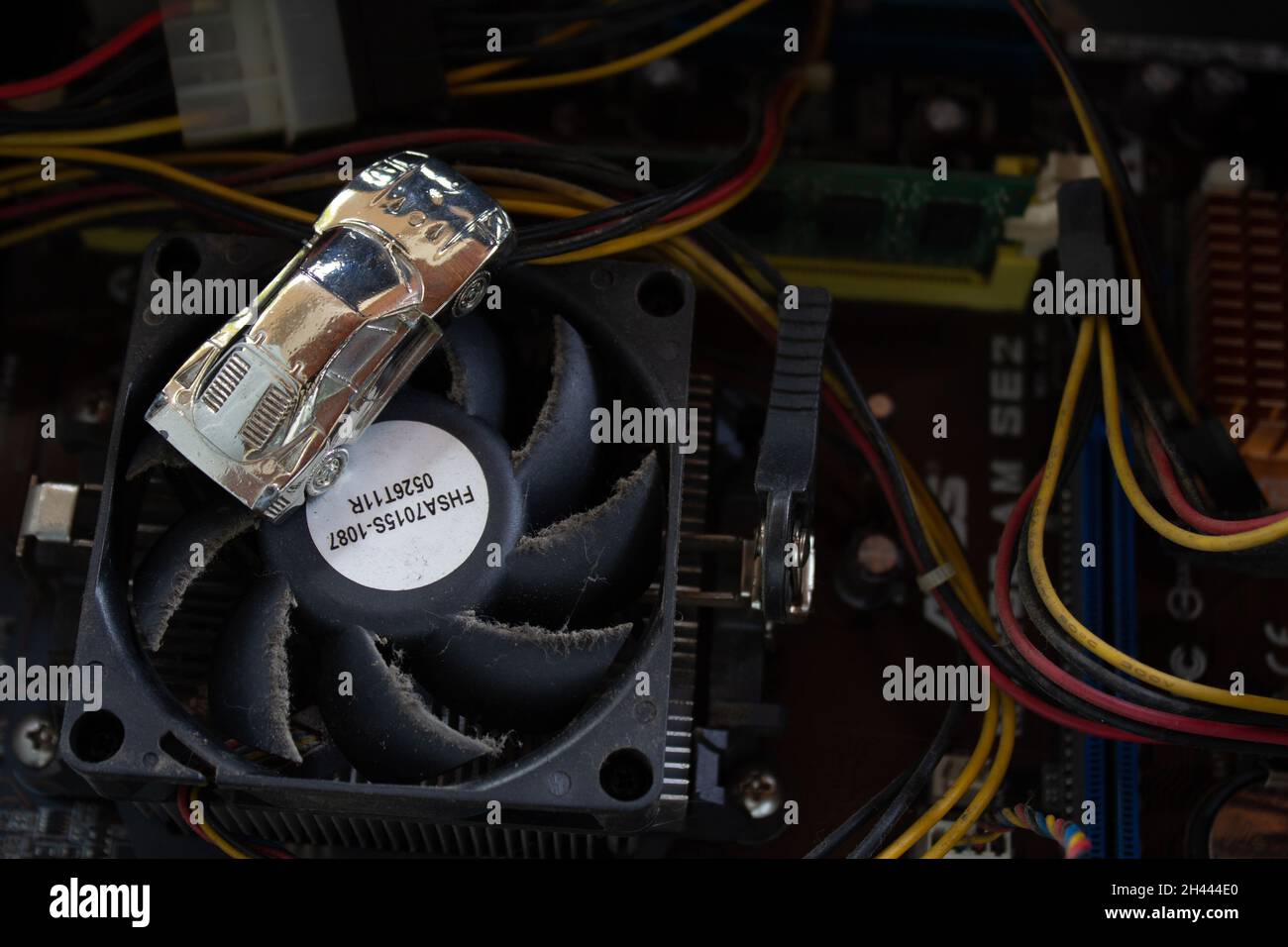 Un'auto in miniatura color argento lucido su una vecchia e sporca ventola di raffreddamento della cpu del computer. Foto Stock