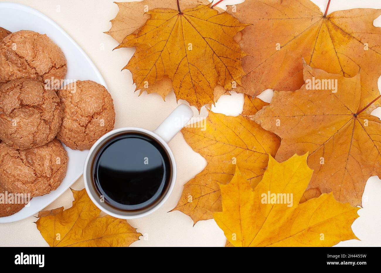 piatto di foglie di acero giallo autunno, tazza con tè caldo, piatto bianco con biscotti su sfondo avorio Foto Stock
