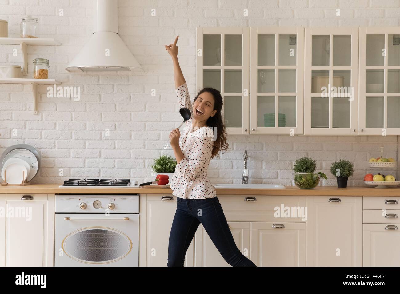 Donna distratta dalla cucina, tiene la siviera cantare danzando in cucina Foto Stock