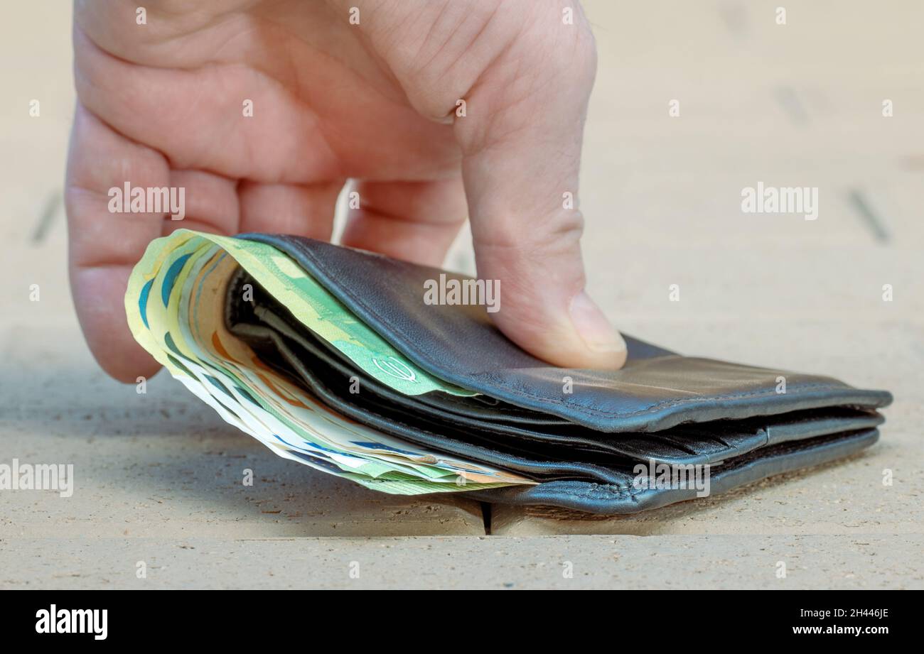 Afferra a mano il portafoglio dal pavimento della strada. Foto Stock