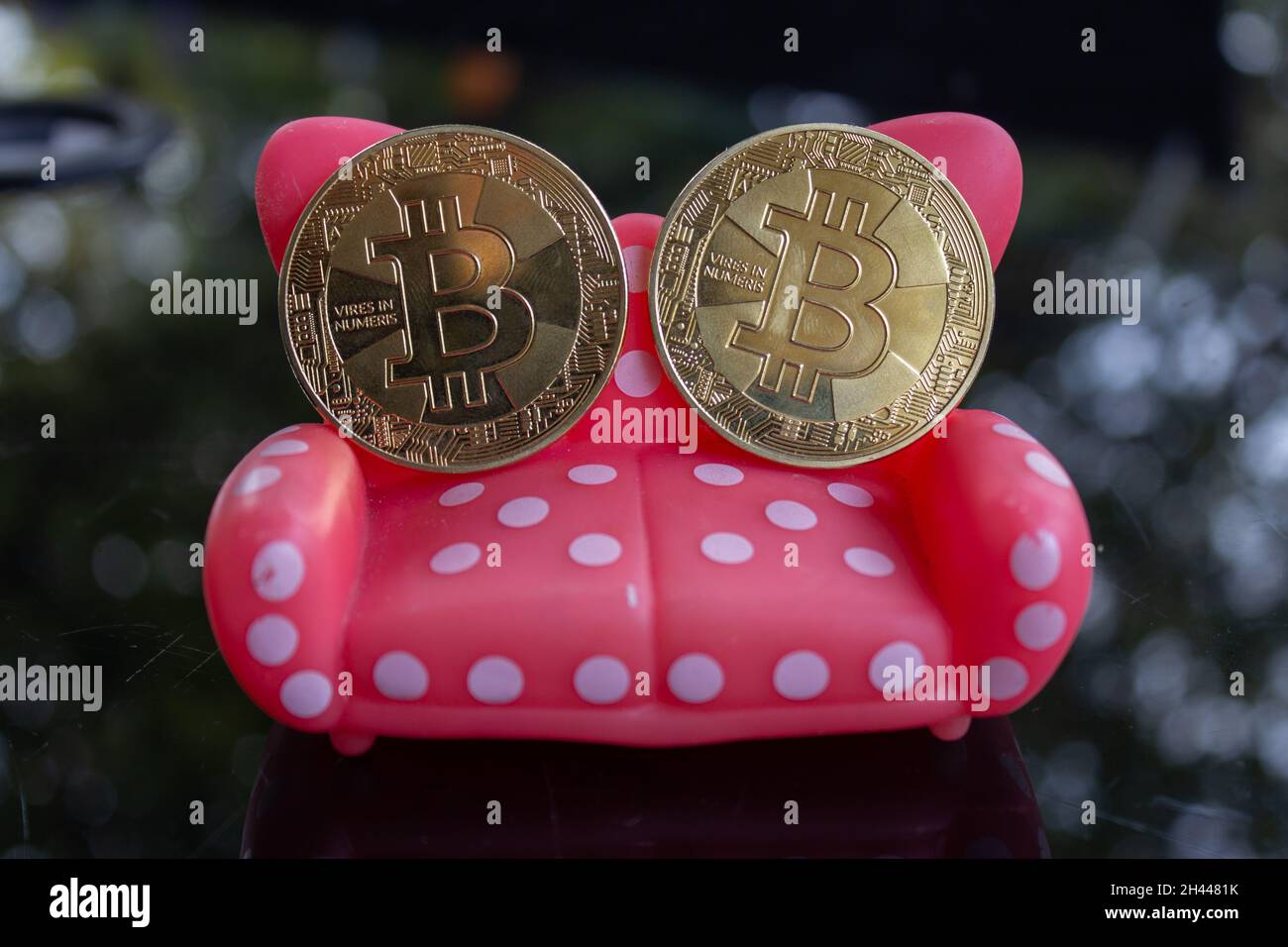 Alcuni bitcoins seduti su un divano giocattolo rosso punteggiato bianco. Conforto soldi e affari. Foto Stock