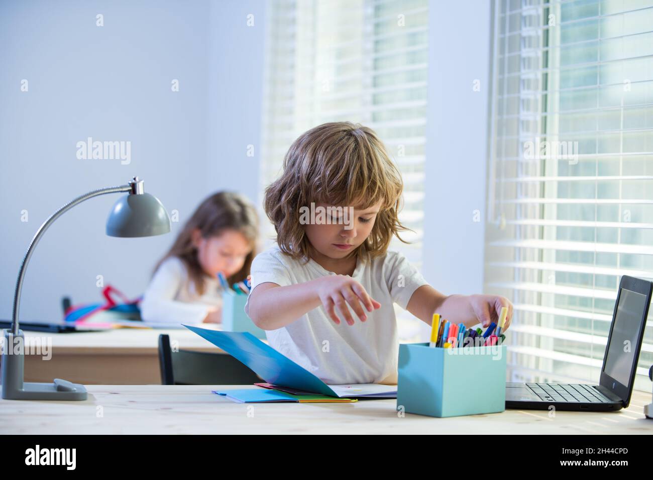 Ragazzo di scuola seduto al tavolo, scrivendo i compiti o preparandosi per l'esame. Bambino pronto per lo studio. Poco apprendimento ostinato. Foto Stock