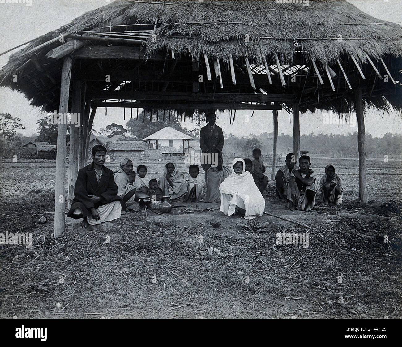 Assam, India: Un centro fuori-paziente di kala-azar: Un piccolo gruppo di uomini, donne e bambini si siedono sotto un riparo erba-coperto con alcune ciotole di metallo (per riscaldare l'acqua per la sterilizzazione?). Fotografia, 1900/1920 (?). Foto Stock