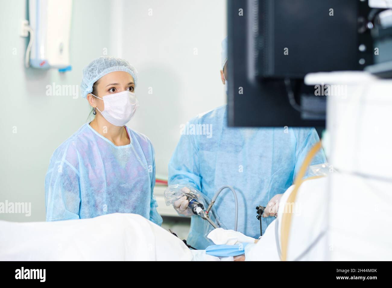 Una giovane dottore in uniforme blu e una maschera protettiva guarda attentamente il monitor durante un intervento chirurgico. Una chirurgo femminile esegue un intervento laparoscopico. Messa a fuoco selettiva. Foto Stock