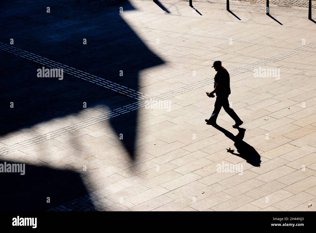 Belgrado, Serbia - 25 ottobre 2020: Un uomo maturo che indossa il cappello che cammina da solo attraverso la piazza lastricata della città, alto angolo di vista con ombre Foto Stock