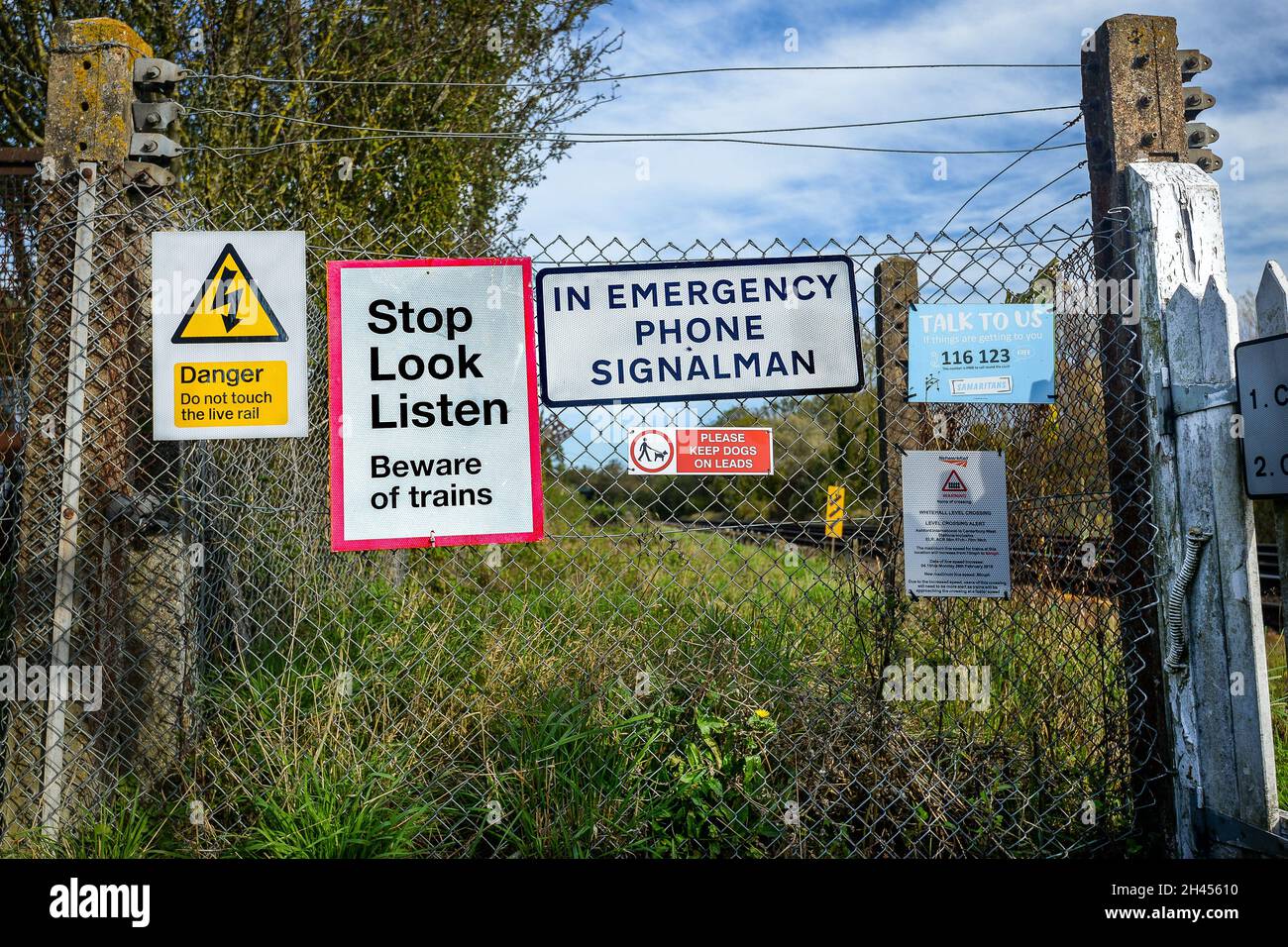 Segnali di avvertimento per l'attraversamento della ferrovia sulla recinzione all'incrocio a livello di campagna. Foto Stock