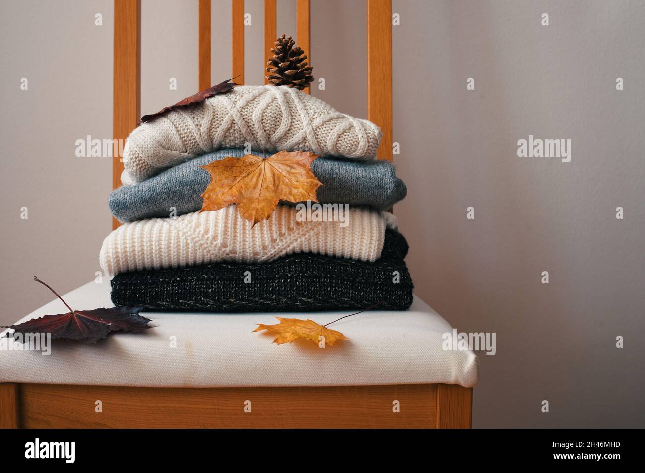 Pila di maglioni caldi a maglia su sedia in legno con foglie secche autunnali e pinecone Foto Stock