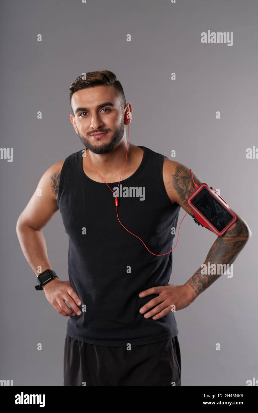Ritratto di allegro sportivo in piedi con le mani sui fianchi, ascoltare musica e guardare la fotocamera Foto Stock