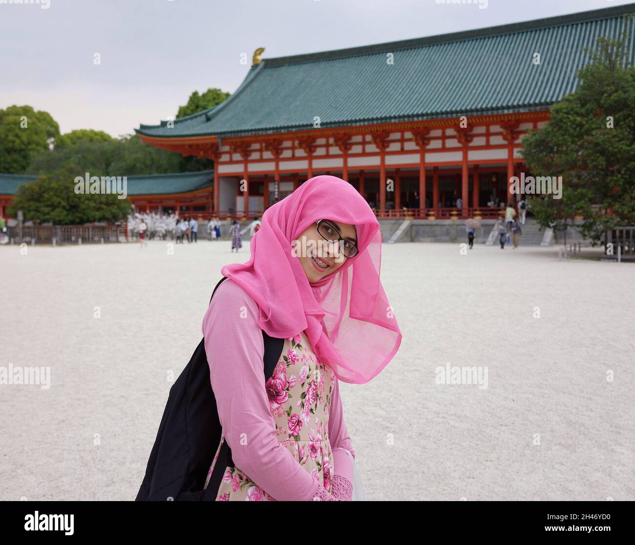 Primo piano ritratto della giovane donna musulmana asiatica che indossa hijab e occhiali nel cortile del santuario heian. Espressione allegra, eccitata e felice. Foto Stock