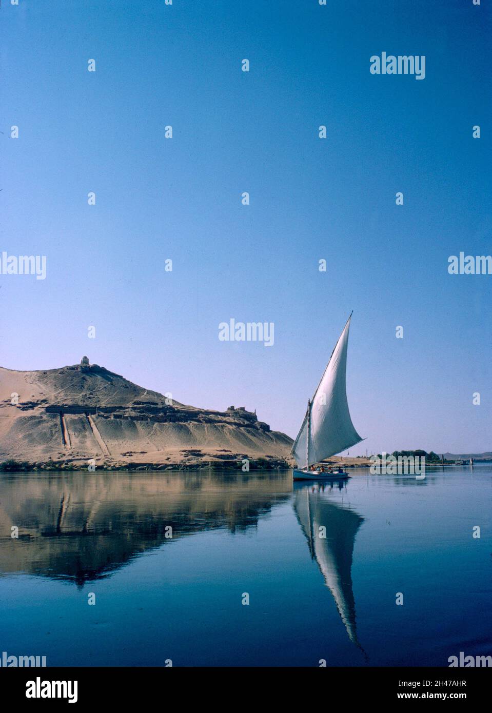 Africa, Egitto, Luxor, fiume Nilo 1976. Una feluca sul Nilo ad Assuan. Tomba sulla collina di Qubbet el Hawa e antiche tombe nella scogliera del deserto. Foto Stock