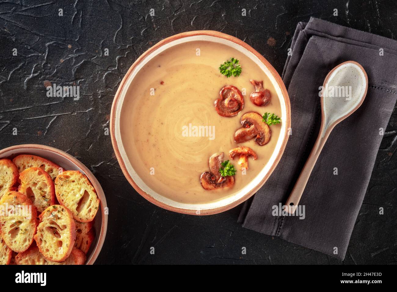 Zuppa di funghi in un recipiente rustico con pane tostato, sparato dall'alto su uno sfondo di ardesia nera Foto Stock