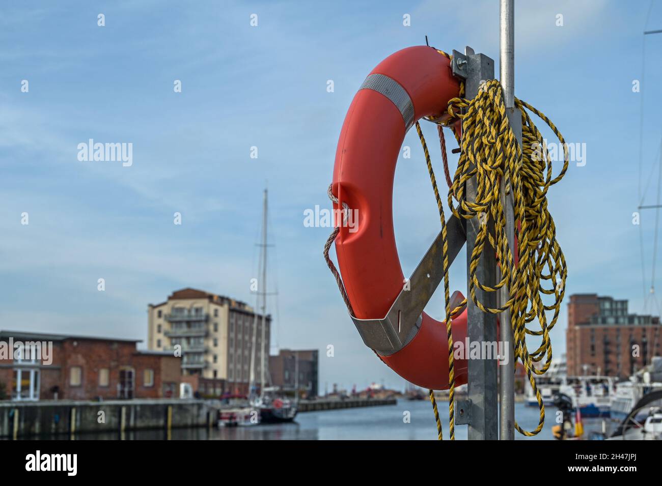 Orange Lifebuoy con corda sul molo nel vecchio porto di Wismar sul Mar Baltico, cielo blu, spazio copia, fuoco selezionato Foto Stock
